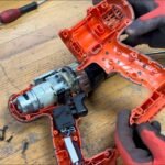 A cordless drill sitting on a workbench awaiting repair in a bright workshop.