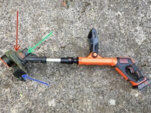 A person inspecting a broken cordless strimmer in a sunny green garden.