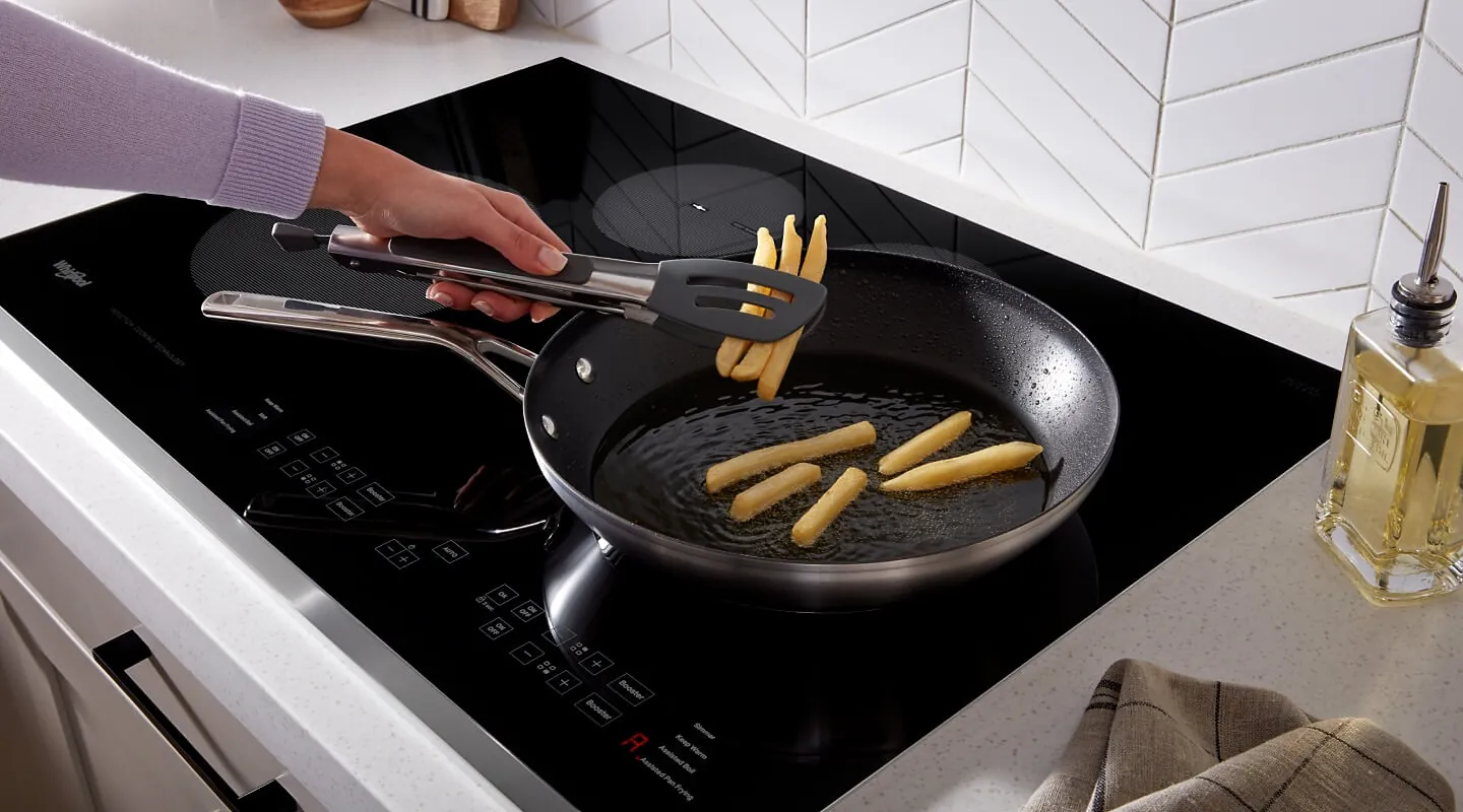 A hand wiping the underside of a pan before placing it on an induction hob.