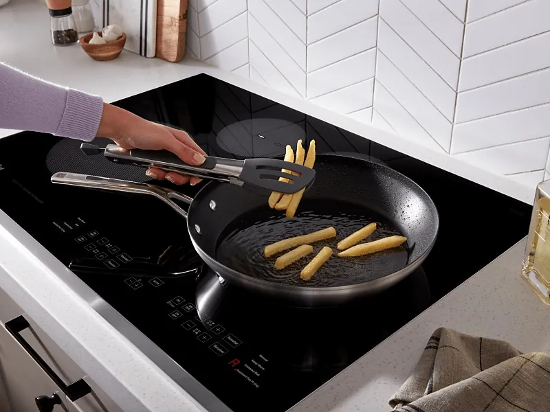 A stainless steel pan base resting flat on a clean induction cooktop surface.
